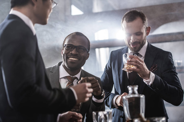 Multiethnic group of businessmen spending time together drinking whiskey and smoking, multicultural business team - Foto, Imagem