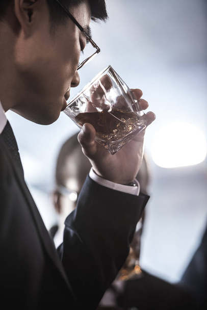 ガラスからウィスキーを飲みながら眼鏡でアジア系のビジネスマンのクローズ アップ ビュー - 写真・画像