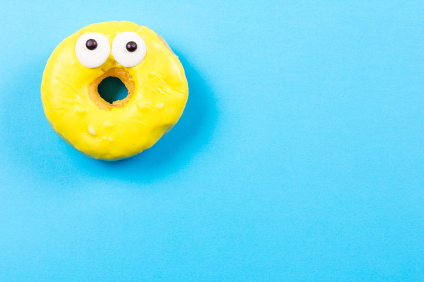 Žlutý kulatý donut s očima na modrém pozadí. Plochá ležel, horní pohled. - Fotografie, Obrázek