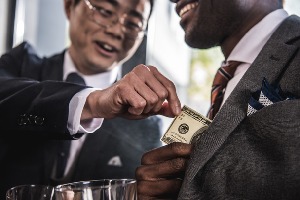 Recortado disparo de dos hombres de negocios sonrientes hablando y sosteniendo billete de dólar
 - Foto, Imagen