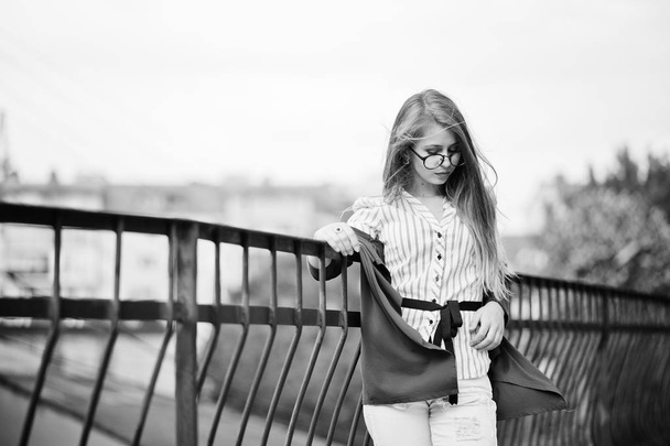 Trendy girl at glasses and ripped jeans against barrier on stree - Foto, Bild