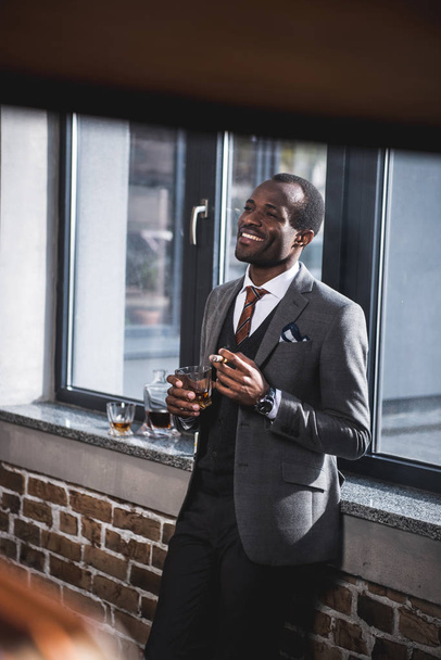 confident businessman holding cigar and glass of alcohol in hands - Foto, afbeelding