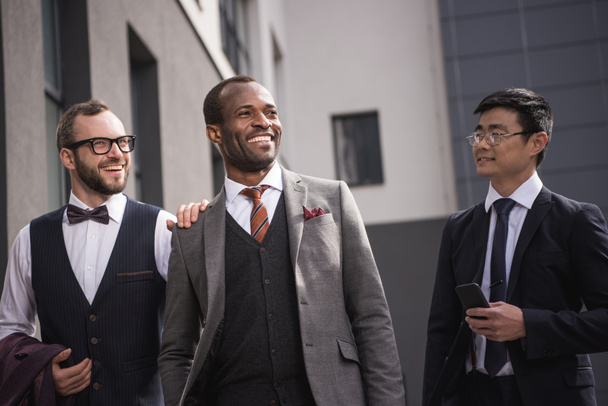 junge stilvolle multiethnische Geschäftsleute in Formalbekleidung, die im Freien spazieren gehen, Besprechung des Geschäftsteams - Foto, Bild