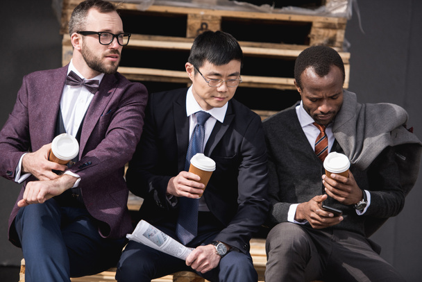 jovens empresários multiétnicos em formalwear sentado em coffee break ao ar livre, reunião de equipe de negócios
 - Foto, Imagem
