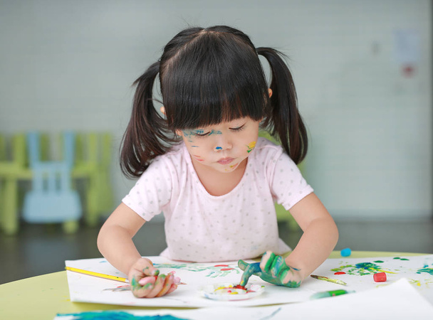 Child girl painting with paintbrush and water colors. Kid activities concept. - Foto, afbeelding