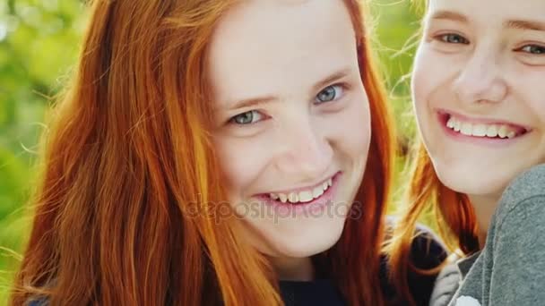 İki mutlu kız ikiz yakın çekim portre. Bak Kızıl saçlı, bunlar fotoğraf makinesi, gülümseme, sarılmak. Güneş güzel saçlarını aydınlatır - Video, Çekim