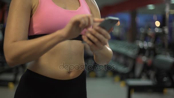 Young female scrolling on mobile phone in gym, setting up training application - Filmagem, Vídeo