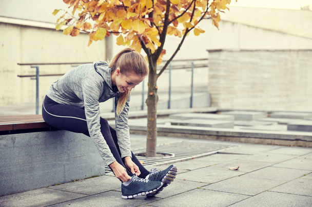 happy young sporty woman tying shoelaces outdoors - Zdjęcie, obraz