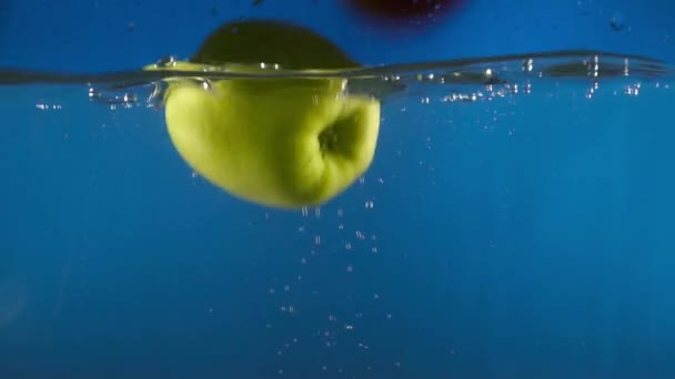 Close-up van groene verse appel vallen in water op de blauwe backgrond slow motion - Video