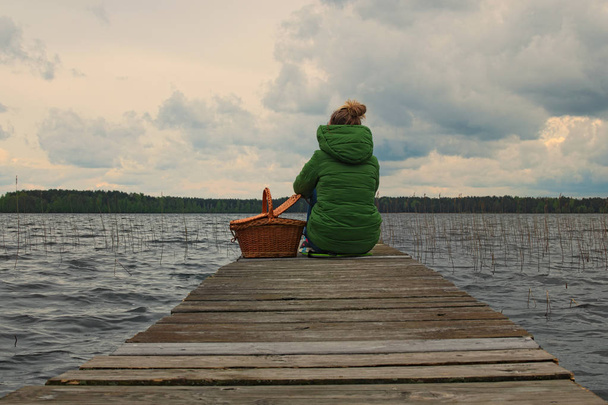  A young girl sits on the edge of a wooden pier and looks into the distance. Volyn region. Ukraine - Photo, Image