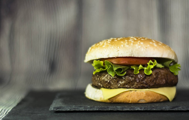 Вкусный гамбургер с сыром, салатом и помидорами на камне
 - Фото, изображение