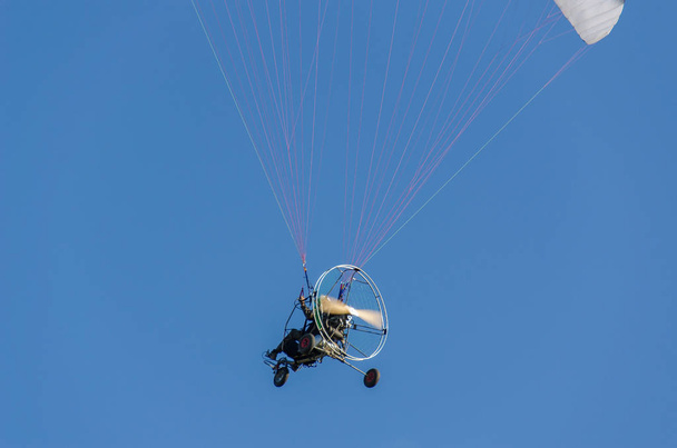 Чоловік на моторному параплані в блакитному небі
 - Фото, зображення