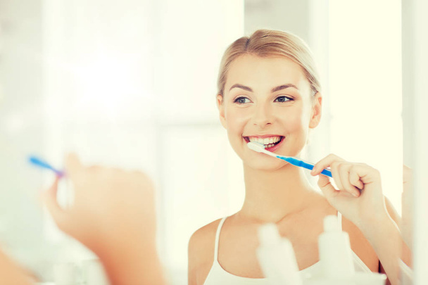 woman with toothbrush cleaning teeth at bathroom - Foto, Bild