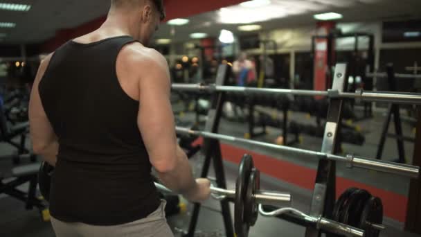 Sportowy facet robi kilka lift-ups z curl bar, wprowadzenie go z powrotem na stoisku w siłowni - Materiał filmowy, wideo