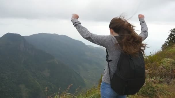 Nuori naispatikoija, jonka reppu ulottuu vuoren huipulle ja nostaa kätensä. Nainen turisti seisoo reunalla kaunis kanjoni, voitokkaasti ojentaen kädet ylös. Hidastettu peruutusnäkymä
 - Materiaali, video