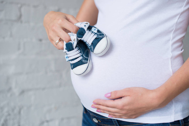 Pregnant girl with baby sneakers on the background of the tummy. - 写真・画像