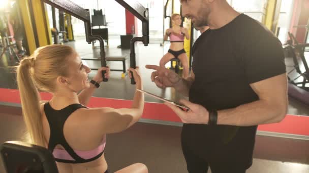 Képzés az edzőteremben, nő, nyíltan flörtöl vele vonzó személyi edző - Felvétel, videó