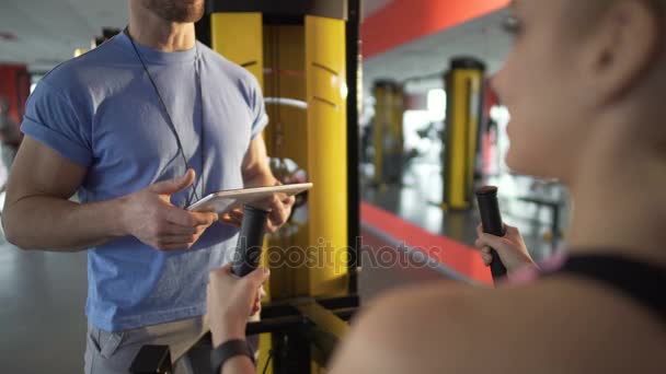 Trainer acquainting client with gym equipment and discussing plan of training - Video