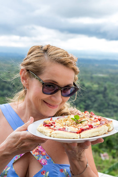 Woman with delicious strawberry pizza on a balinese tropical nature background. Bali island, Indonesia. - Photo, Image