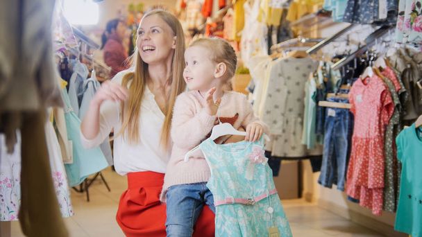 молодая мать с дочкой веселятся в магазине детской одежды
 - Фото, изображение