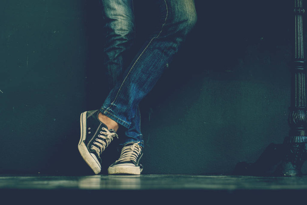 Young fashion man's legs in blue jeans and black sneakers on wooden floor. - Photo, Image