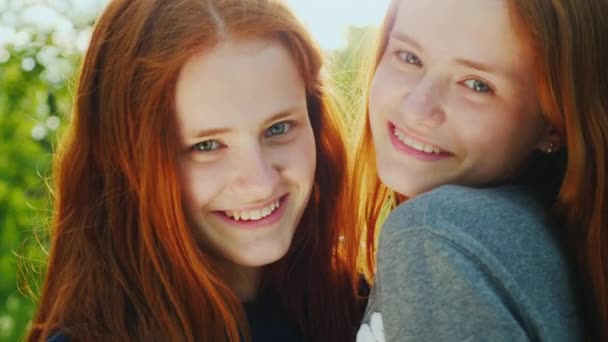 Πορτραίτο των διδύμων δύο αδελφές της εφηβείας. Είναι κοκκινομάλλα, κοιτάξτε την κάμερα, το χαμόγελο, το αγκάλιασμα. Ο ήλιος φωτίζει όμορφα μαλλιά τους - Πλάνα, βίντεο