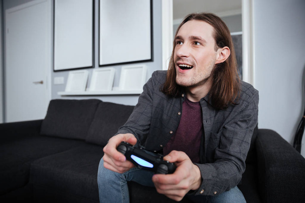 Ευτυχισμένος άνθρωπος gamer κάθεται στο σπίτι σε εσωτερικούς χώρους και να παίζουν παιχνίδια - Φωτογραφία, εικόνα