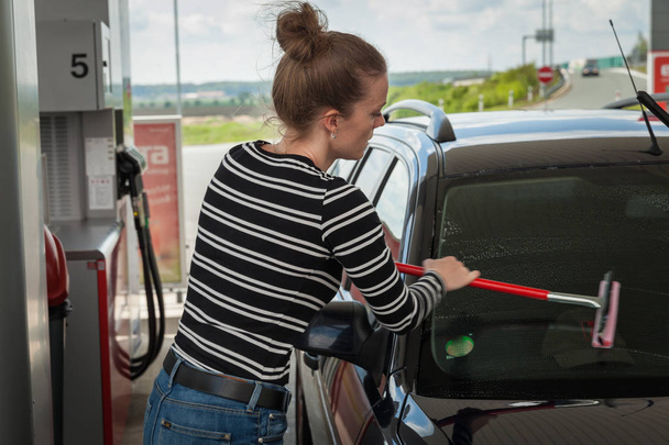 Jovem mulher lavando o copo de um carro em um posto de gasolina
 - Foto, Imagem