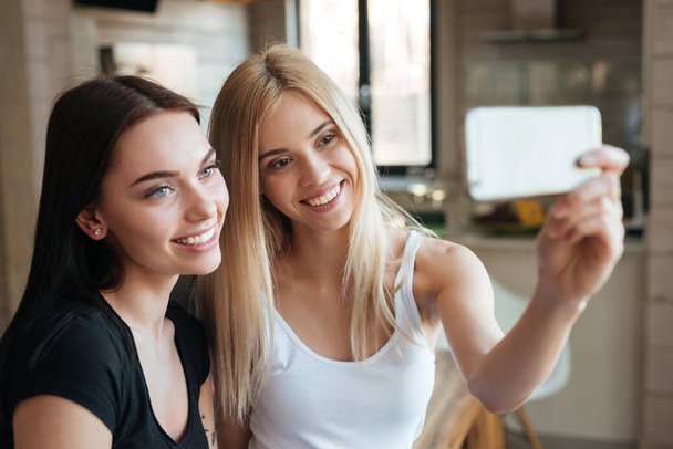 Les jeunes deux femmes heureuses assis à la maison à l'intérieur font selfie
 - Photo, image