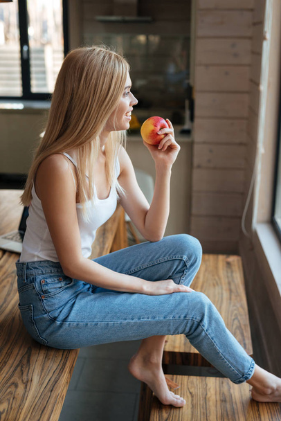 Beautiful young lady sitting at home indoors eating apple - Fotoğraf, Görsel
