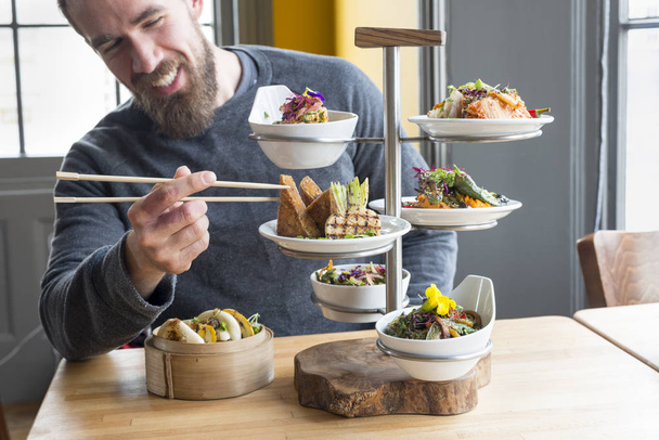 Человек выбирает жареный тофу с помощью палочек из тарелки в ресторане
 - Фото, изображение