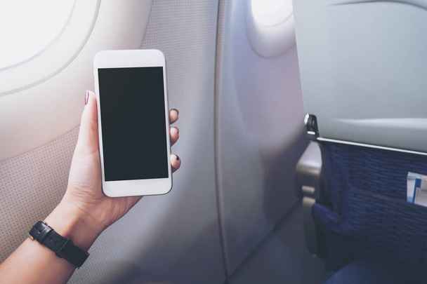 Egy kéz, gazdaság, és nézte a fehér szúró telefon fekete képernyő mellett repülőgépen ablak makett képe  - Fotó, kép