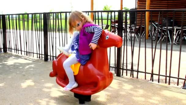 Маленькая девочка, катающаяся на качающейся лошади на детской площадке
 - Кадры, видео