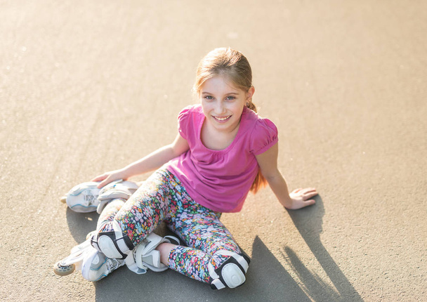girl rollerblading sitting on asphalt, stretching - Photo, image
