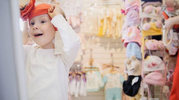 das Mädchen probiert orangefarbene Baskenmütze vor dem Spiegel an - Foto, Bild