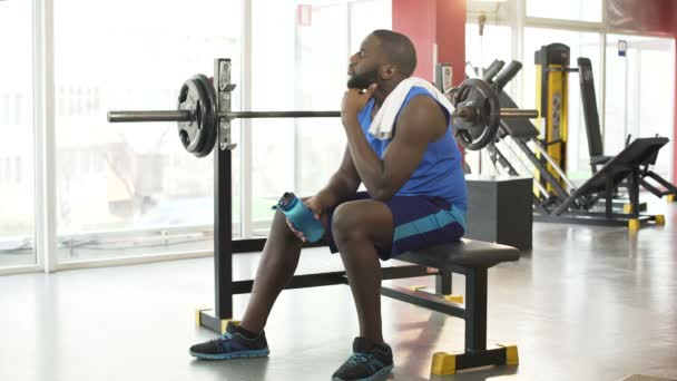 Müder afroamerikanischer Mann sitzt nach aktivem Training auf Trainingsgeräten - Filmmaterial, Video