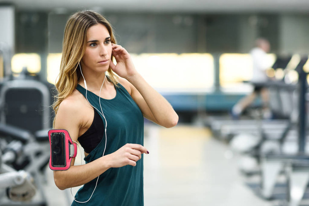 Νεαρή γυναίκα χρησιμοποιώντας smartphone στέκεται στο γυμναστήριο - Φωτογραφία, εικόνα
