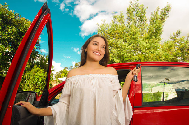 Красива молода жінка тримає ключі і посміхається поруч зі своєю власною червоною машиною
 - Фото, зображення