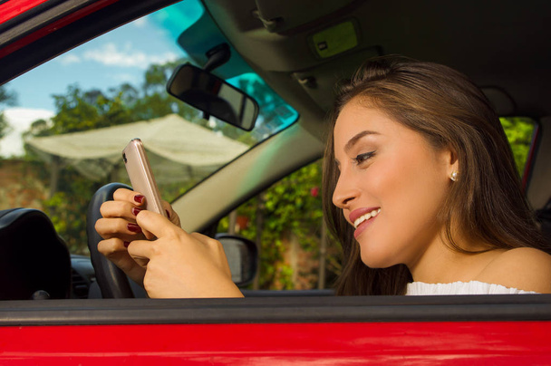 Nahaufnahme einer schönen sexy jungen Frau im roten Auto, die ihr Handy benutzt und lächelt - Foto, Bild
