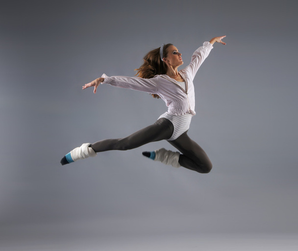 Young, attractive, sporty and sexy modern dancer jumping over grey background - Foto, afbeelding