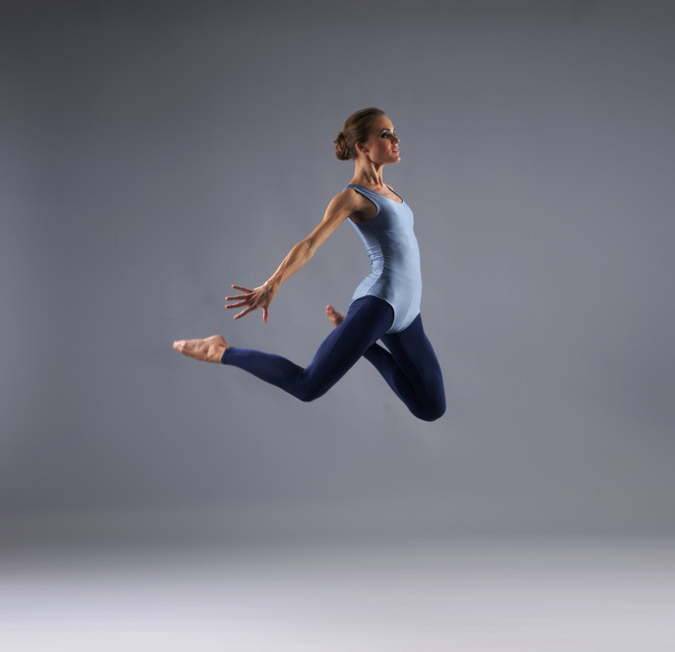 Young, attractive, sporty and sexy modern dancer jumping over grey background - Foto, afbeelding