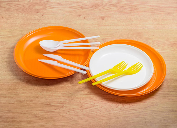 Oranje en witte wegwerp plastic platen, lepels, vorken en messen  - Foto, afbeelding