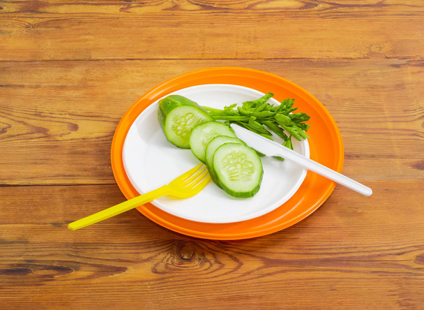Plakjes komkommer op wegwerp plastic platen, mes en vork - Foto, afbeelding