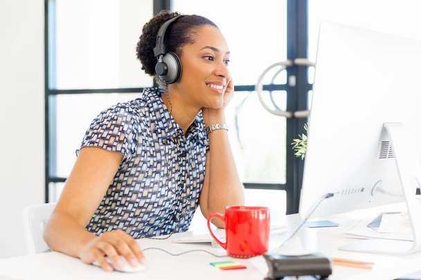 Portrait of smiling afro-american office worker sitting in offfice with headphones - Foto, immagini