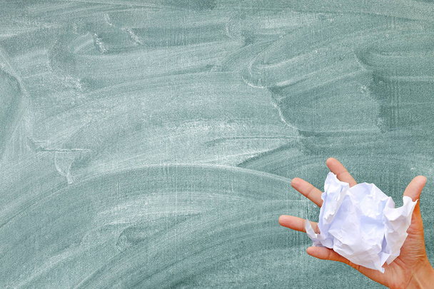 Hand holding crumpled paper against blackboard background. - Foto, imagen
