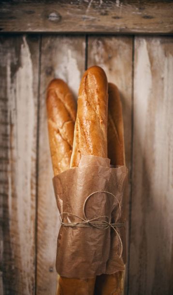 Fresh baguettes in paper on wooden background - Foto, afbeelding