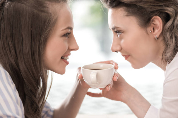 jonge glimlachend vriendinnen koffie drinken - Foto, afbeelding