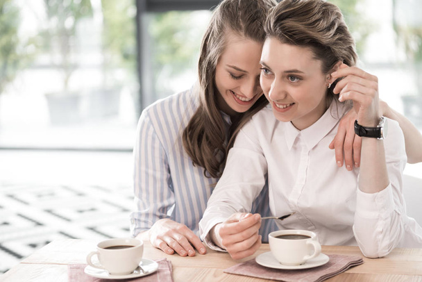 smiling girlfriends drinking coffee and embracing - Фото, зображення