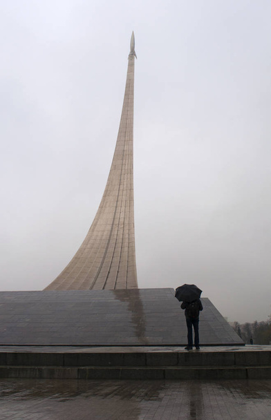 Moscow, Russia: man with umbrella in front of the Monument to the Conquerors of Space, a rocket on his launch ramp built in 1964 to celebrate achievements of the Soviet people in space exploration, inside whose base is the Museum of Cosmonautics  - Photo, Image