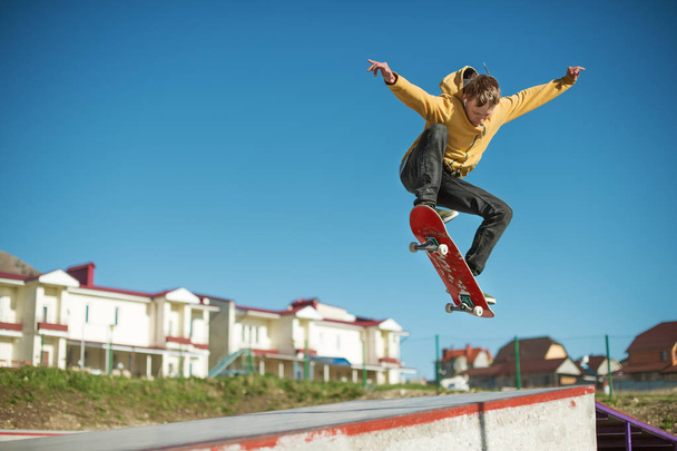 A teenager skateboarder does an ollie trick in a skatepark on the outskirts of the city - Zdjęcie, obraz